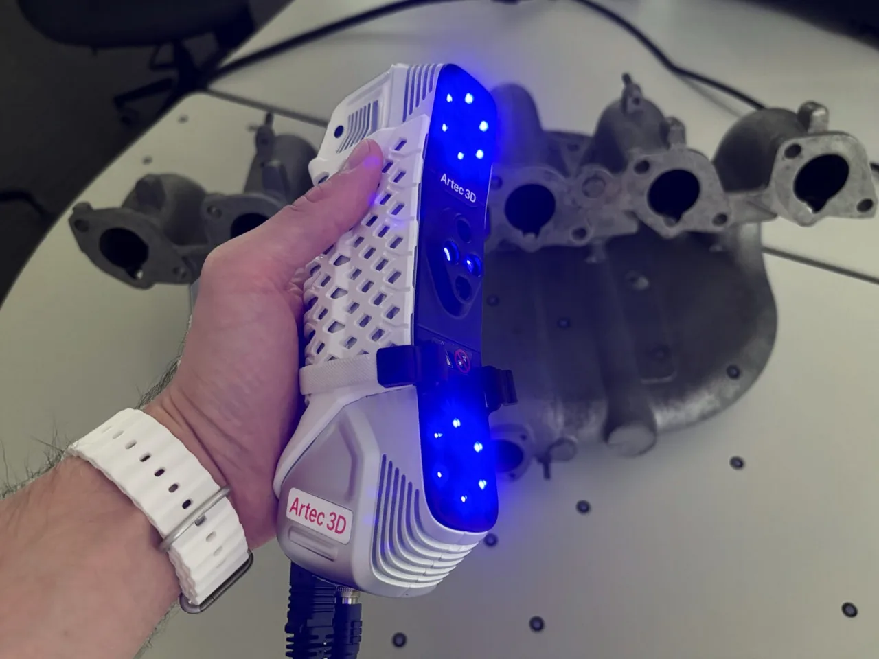 Artec Point scanning a metal component with blue laser lines
